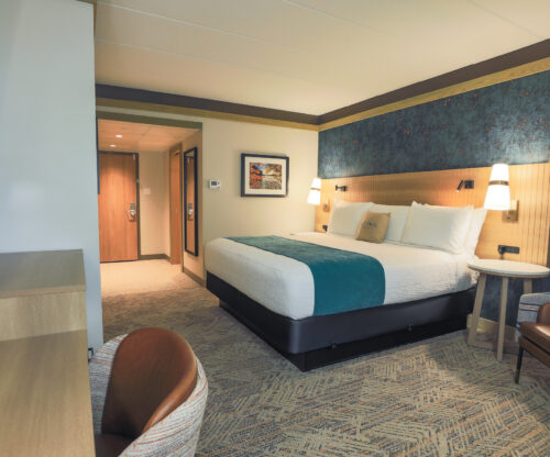 A guest room with a king bed. There is a large wooden headboard with two lamps hanging from it on either end. 